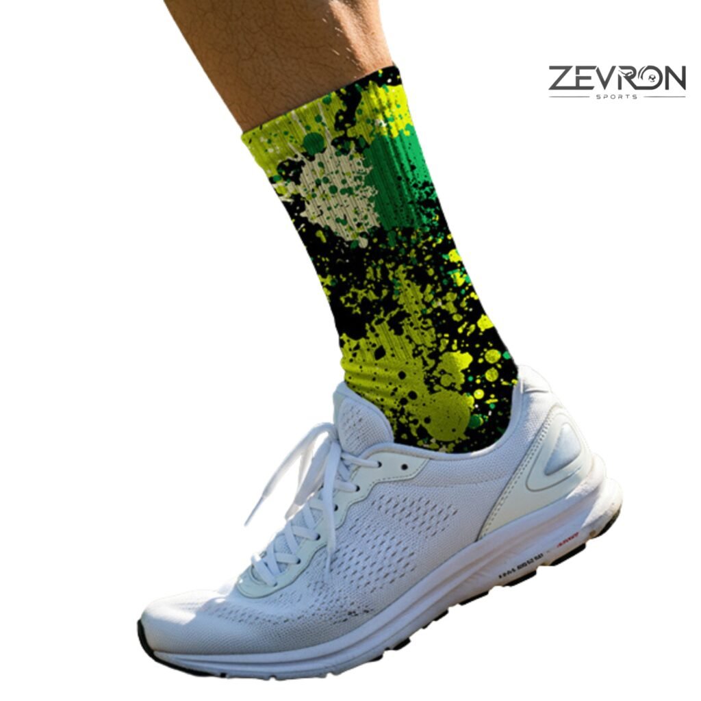 A close-up side profile of a runner's leg wearing a white athletic sneaker and a vibrant Zevron Sports crew sock. The sock features a neon green, lime, and black paint-splatter pattern. The Zevron Sports logo is visible in the upper right corner.